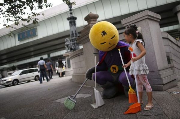 An unidentified man, who calls himself Mangetsu-man (Mr. Full Moon), pauses as he cleans Nihonbashi bridge using a broom with a volunteer in Tokyo