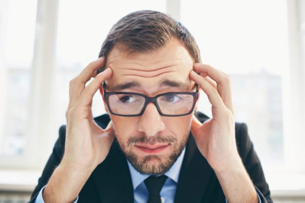 Frustrated businessman in eyeglasses touching his head