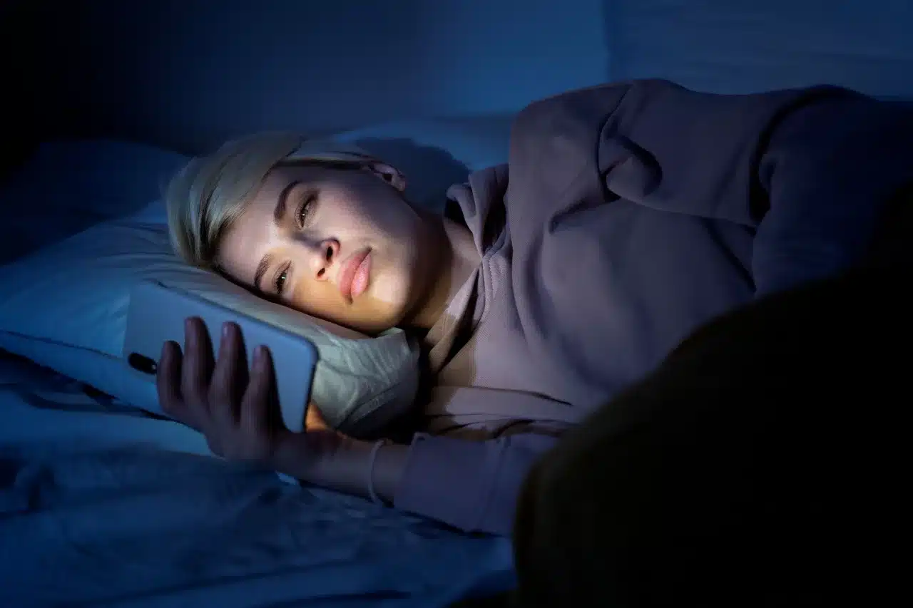 Pessoa acordada de madrugada olhando o celular, representando o hábito de dormir tarde