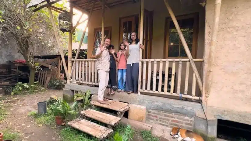Misbah Dwiyanto e família diante da casa construída com terra e bambu